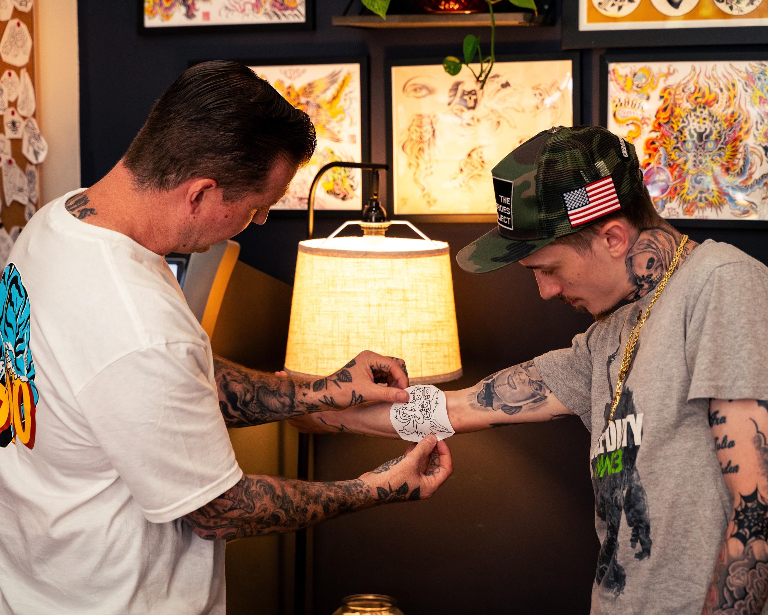 Mike Stapleton placing a stencil on a client’s forearm under a warm lamp